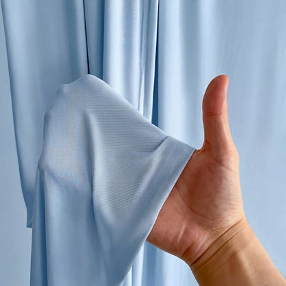 A hand holding a fold of the sky blue fabric, showing its thin, soft texture.